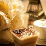 Kawa z kremową pianką i deserem obok białych róż na stole