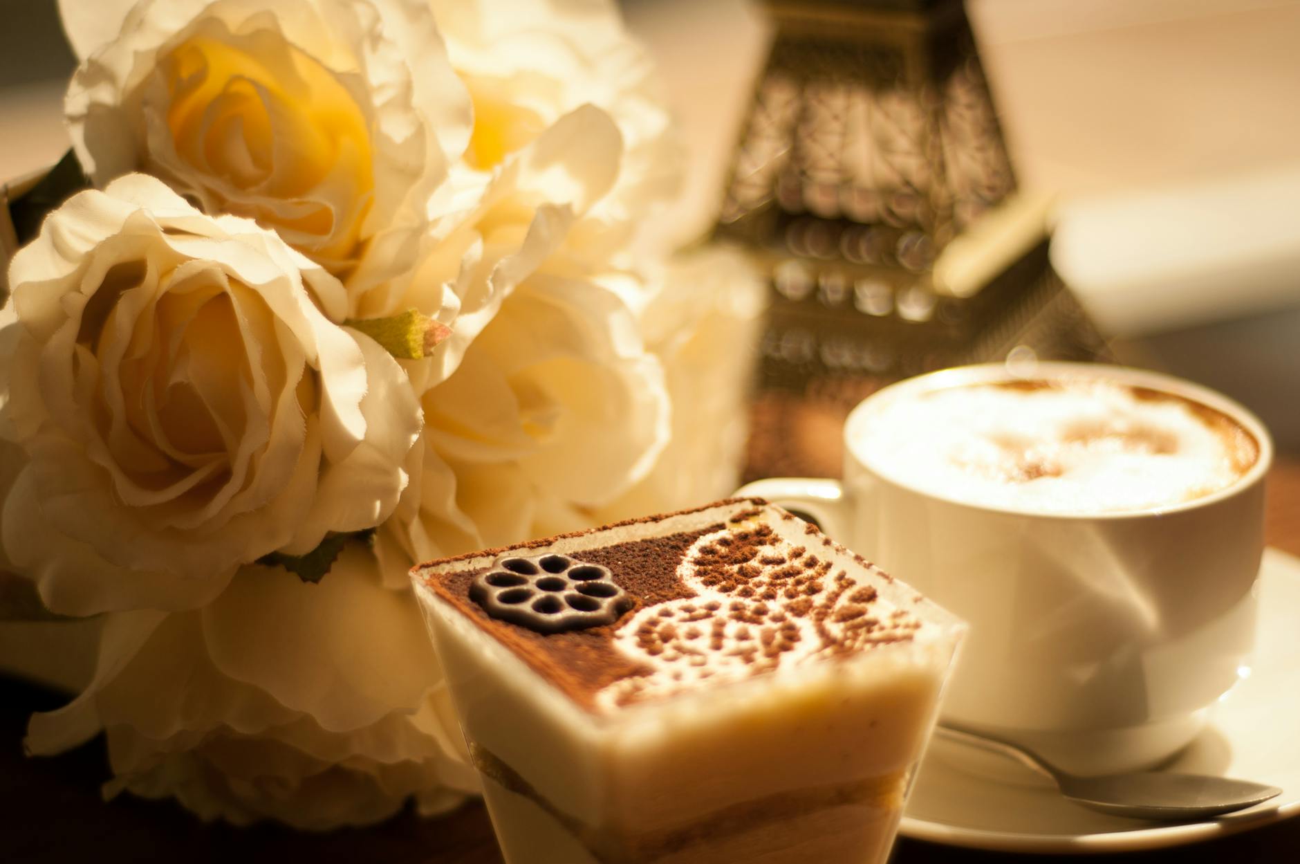 Kawa z kremową pianką i deserem obok białych róż na stole