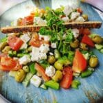 Kolorowa sałatka z fetą, oliwkami, pomidorami i papryką na niebieskim talerzu