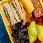 Kolorowe pudełko lunchowe z kanapką, owocami i batonikiem śniadaniowym