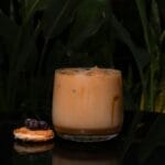 Mrożona kawa z ciastkiem i owocami na ciemnym blacie wśród zielonych roślin