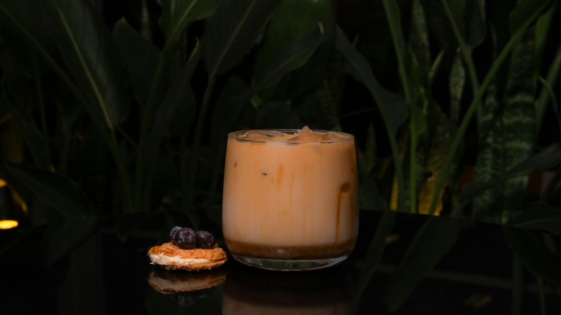 Mrożona kawa z ciastkiem i owocami na ciemnym blacie wśród zielonych roślin