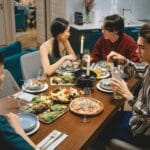 Przyjaciele przy stole zajadają azjatyckie dania i popijają wino