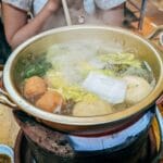 Garnek z gorącym bulionem warzywnym z pulpetami na kuchence